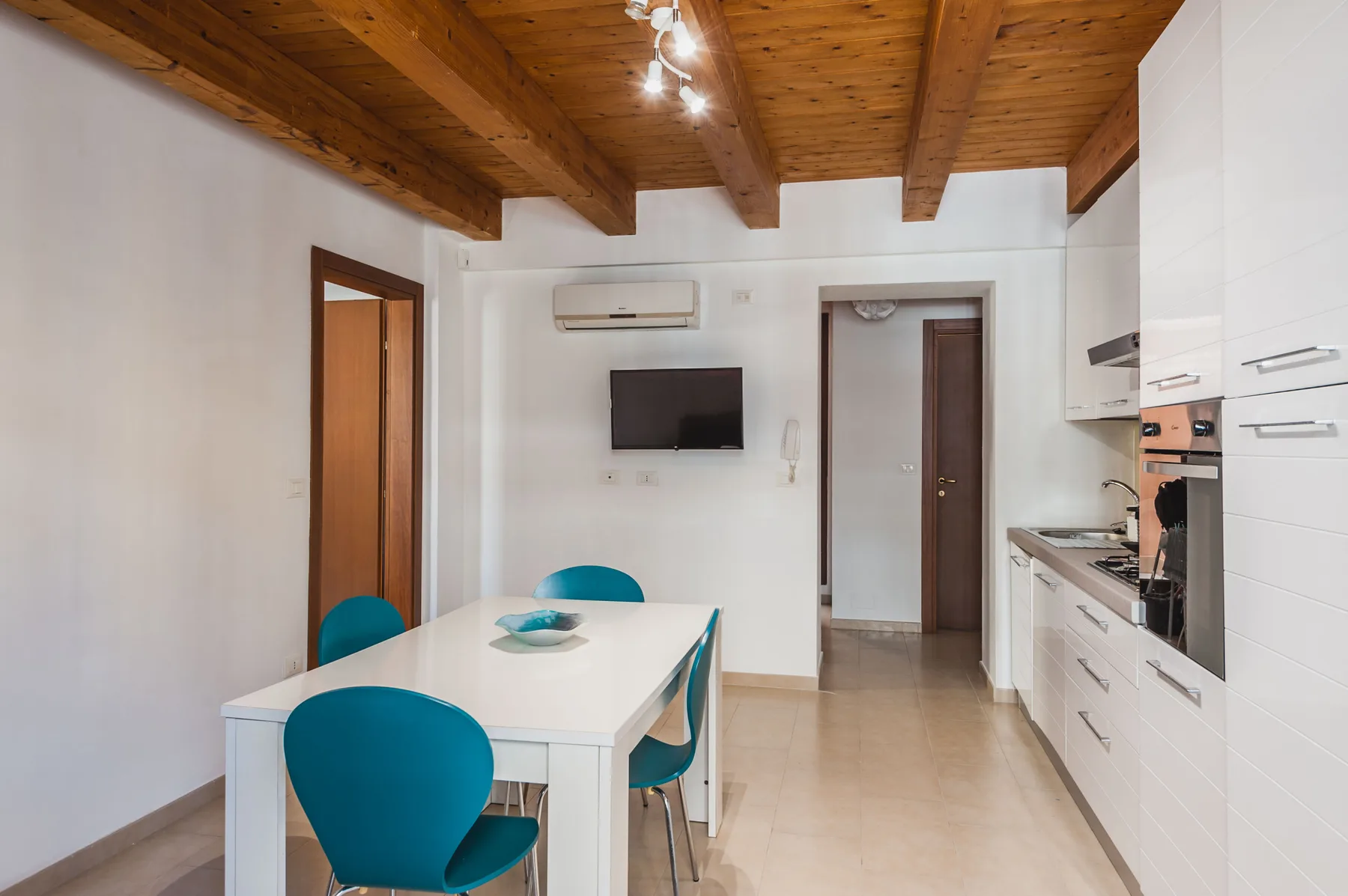 Comedor con una mesa blanca y asientos azules junto a una cocina.