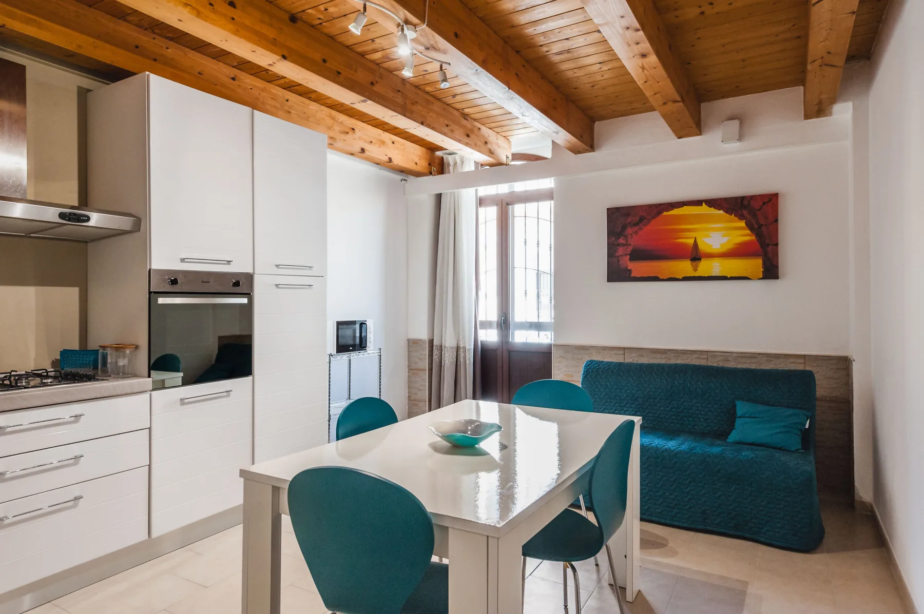 Un comedor con una mesa blanca y asientos color turquesa junto a una cocina compacta.