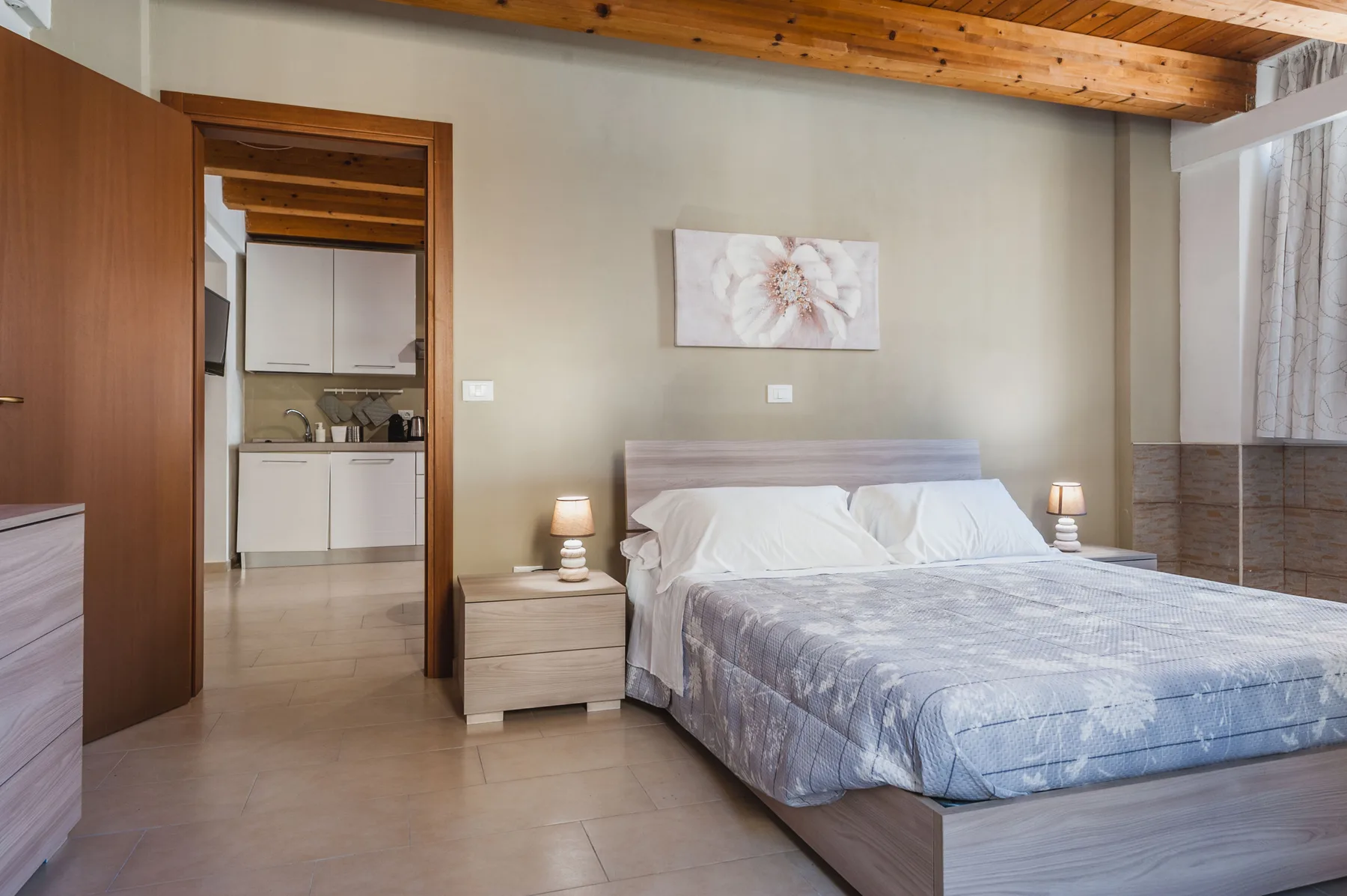 Un dormitorio con una cama, mesitas de noche y una puerta abierta a una pequeña cocina.