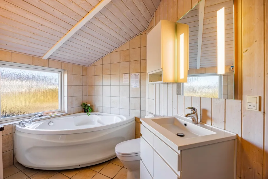 Un baño alicatado con bañera de esquina, lavabo y techo inclinado.