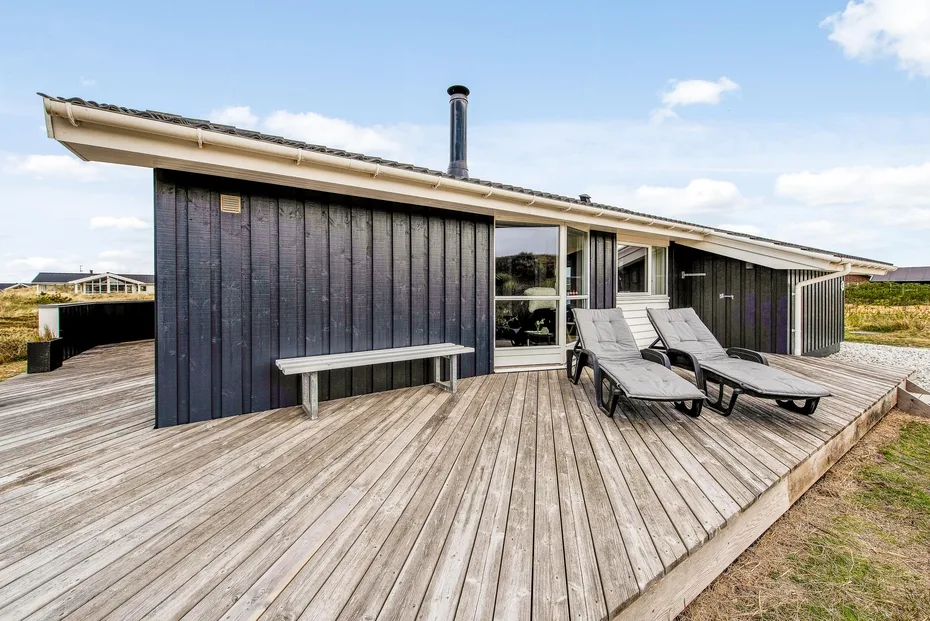 Una casa moderna se abre a una amplia terraza de madera con asientos al aire libre.
