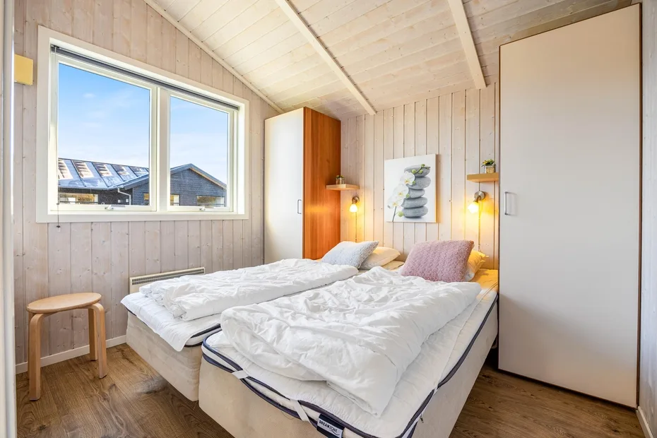 Un dormitorio luminoso con dos camas bajo un techo inclinado revestido de madera.