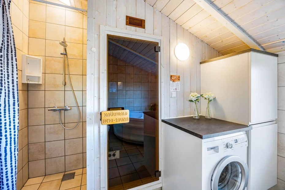 Un baño con azulejos y una ducha junto a una lavadora.