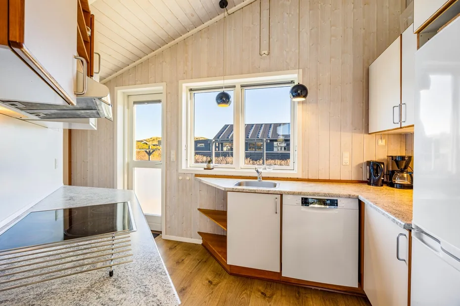 Una cocina luminosa con gabinetes blancos, una placa de cocina y una ventana sobre el fregadero.
