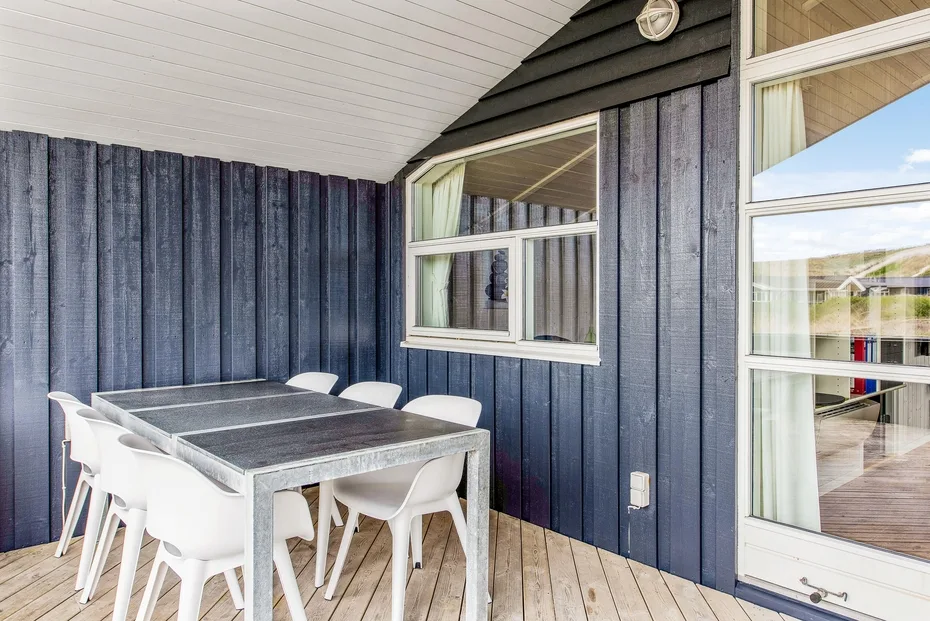 Un patio cubierto con una mesa de comedor y asientos blancos junto a un revestimiento azul oscuro.