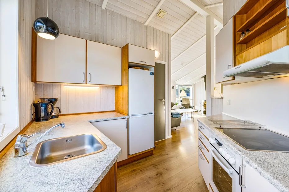 Una cocina compacta con gabinetes claros, un refrigerador y piso de madera.
