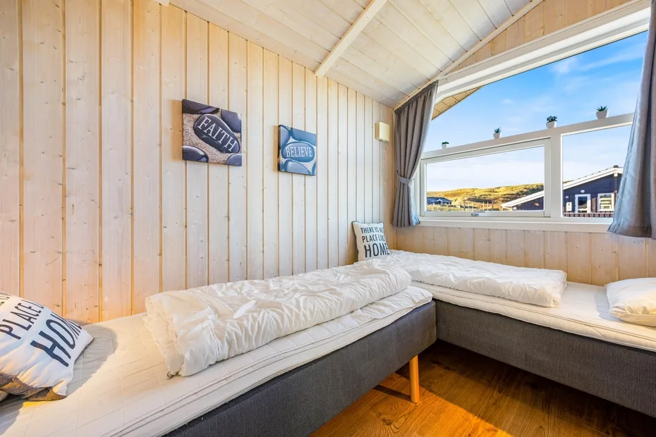Un dormitorio luminoso tiene una cama en L bajo una ventana grande.