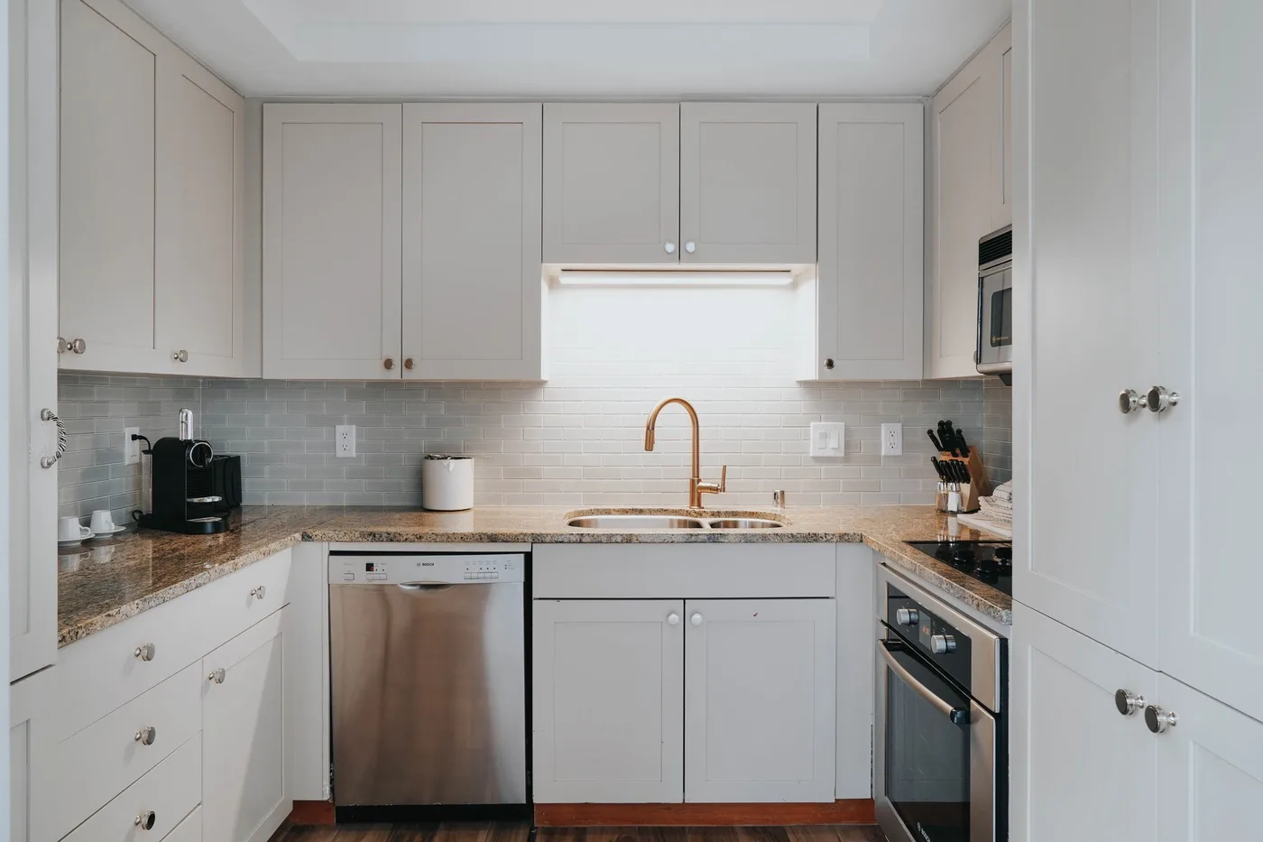 A bright kitchen with pale cabinetry, a central sink, and stainless steel appliances.