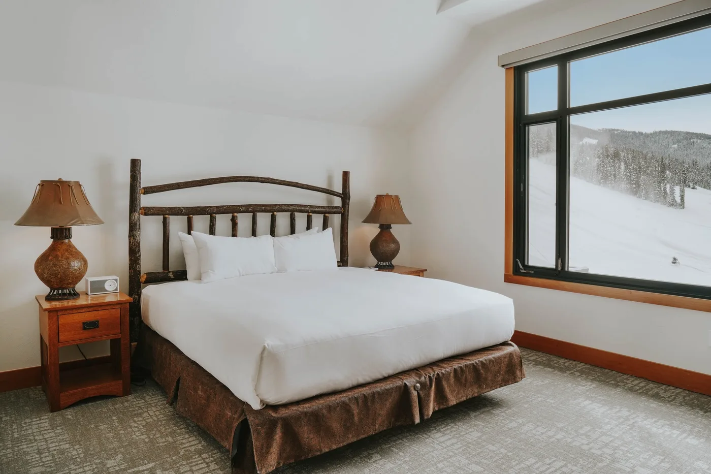 A bedroom with a bed, matching bedside tables, and a large window.