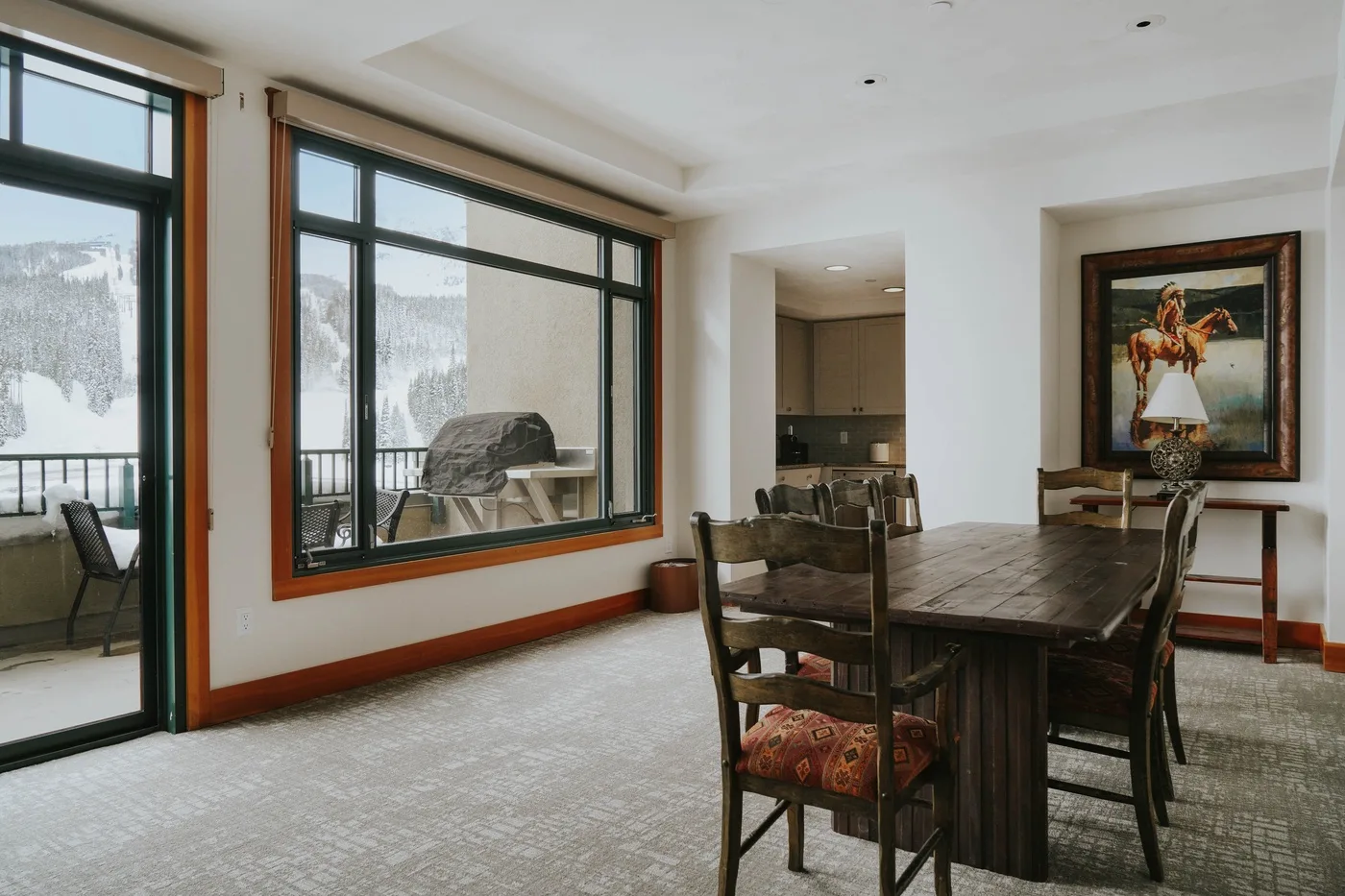 A dining area with a wooden table and large windows overlooking a snowy landscape.