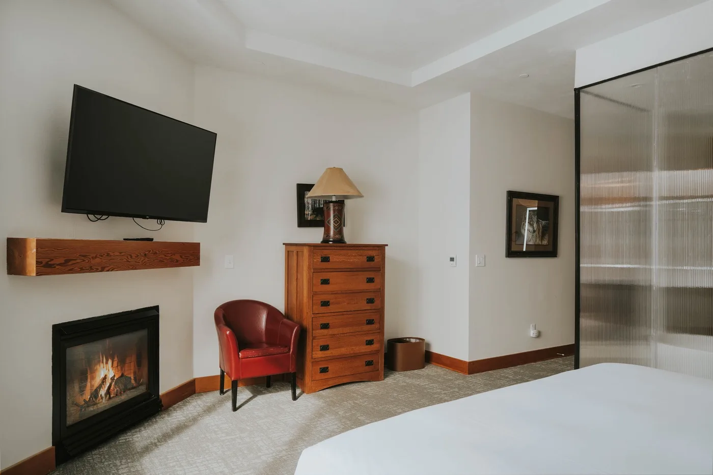 A bedroom with a fireplace, television, dresser, and red seating.