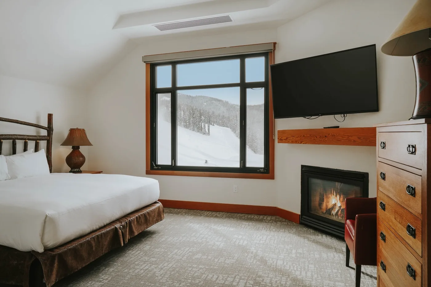 A bedroom with a bed beside a large window overlooking a snowy landscape.