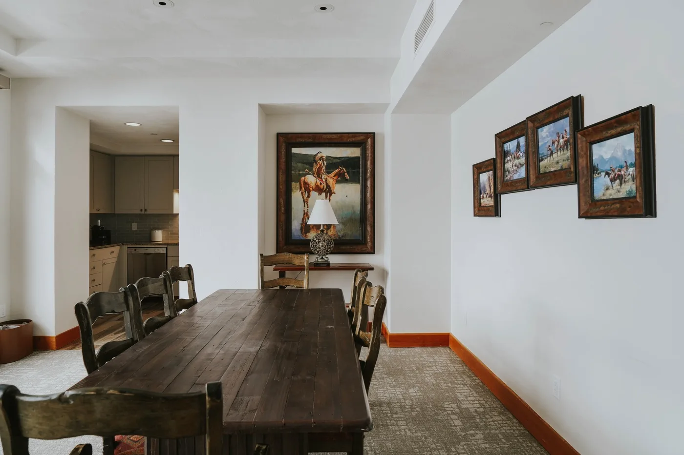 A dining room with a long wooden table, chairs, and framed artwork on the walls.