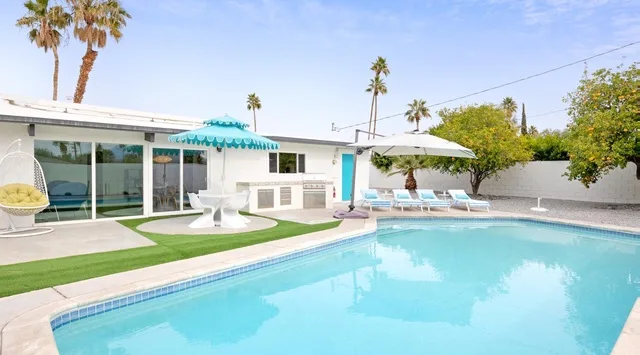 Una piscina junto a una casa blanca, con asientos bajo sombrillas.