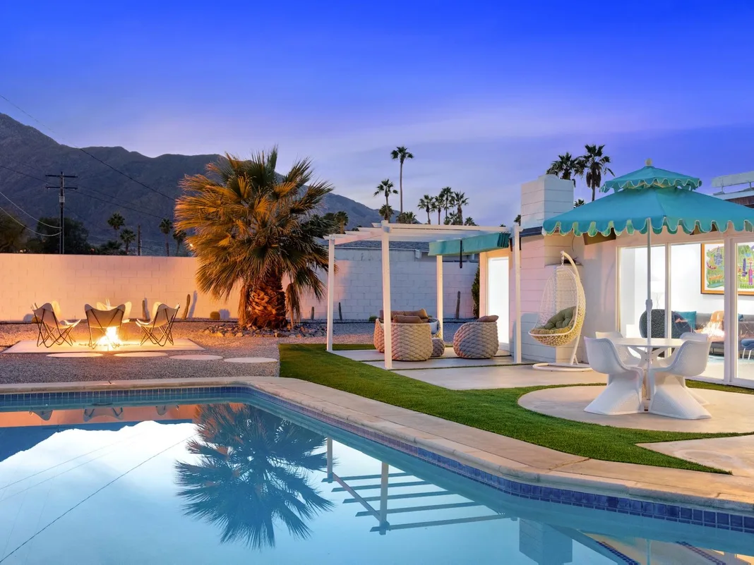 Una piscina al aire libre junto a un patio cubierto con asientos y palmeras.