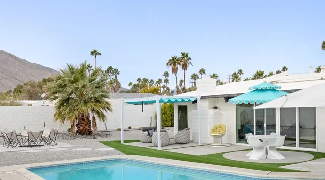 Una piscina junto a un edificio blanco moderno con asientos al aire libre a la sombra.