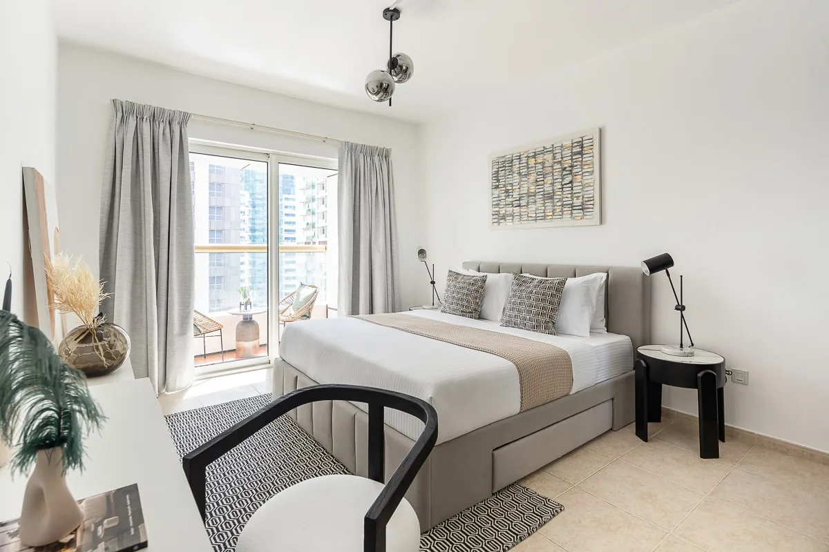 A bright bedroom with a large bed, gray curtains, and a balcony window.