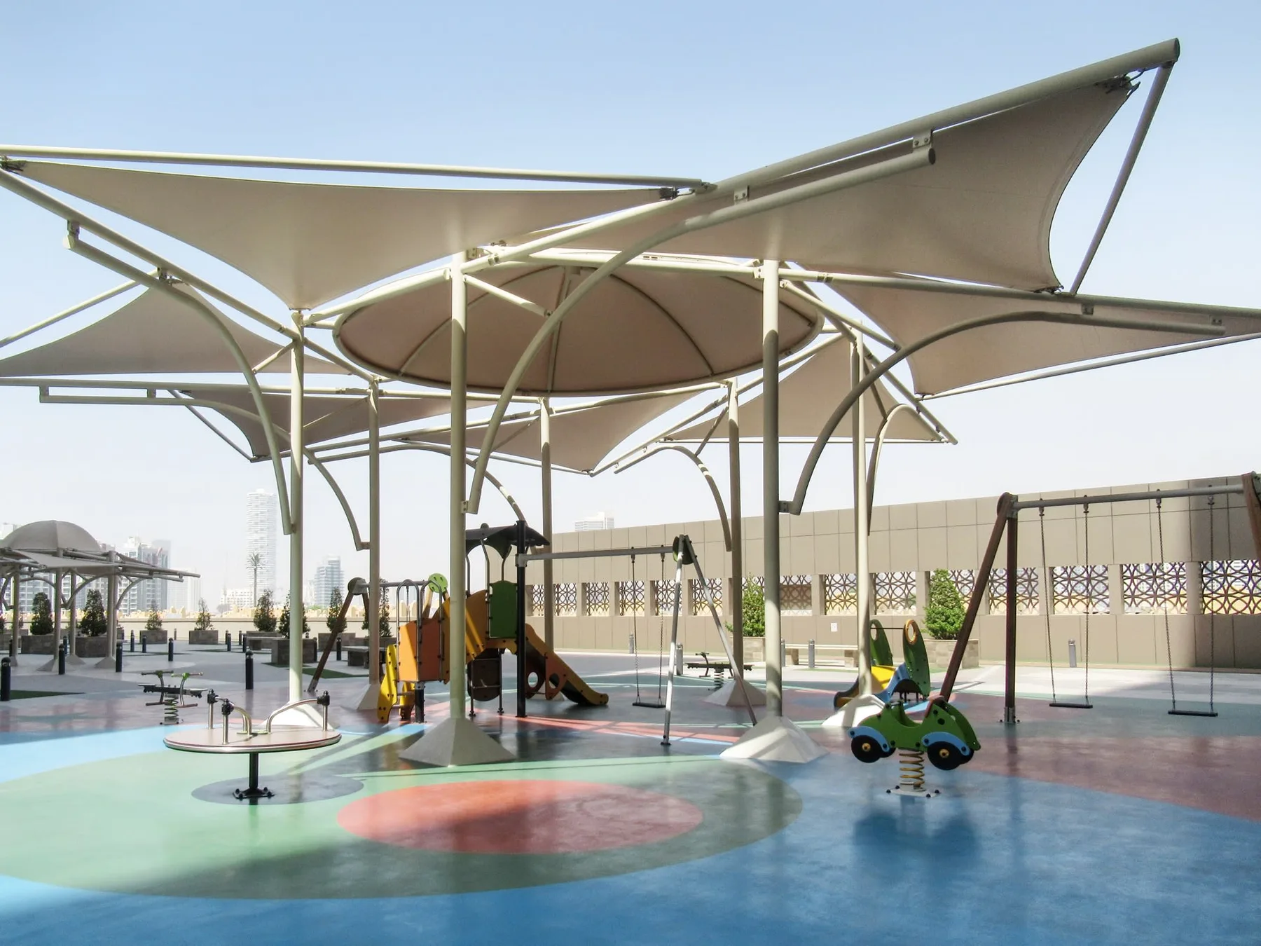 An outdoor playground with colorful play equipment beneath large shade canopies.