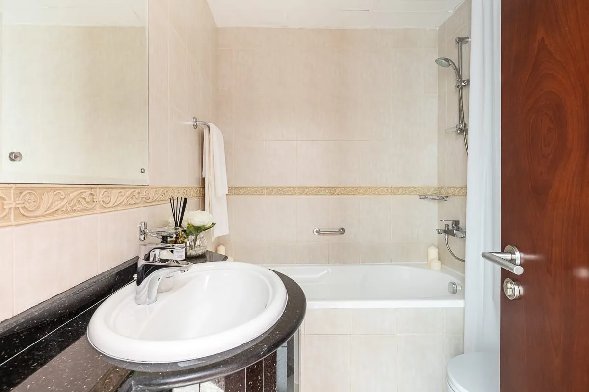 A bathroom with a sink and bathtub beneath a decorative tile border.
