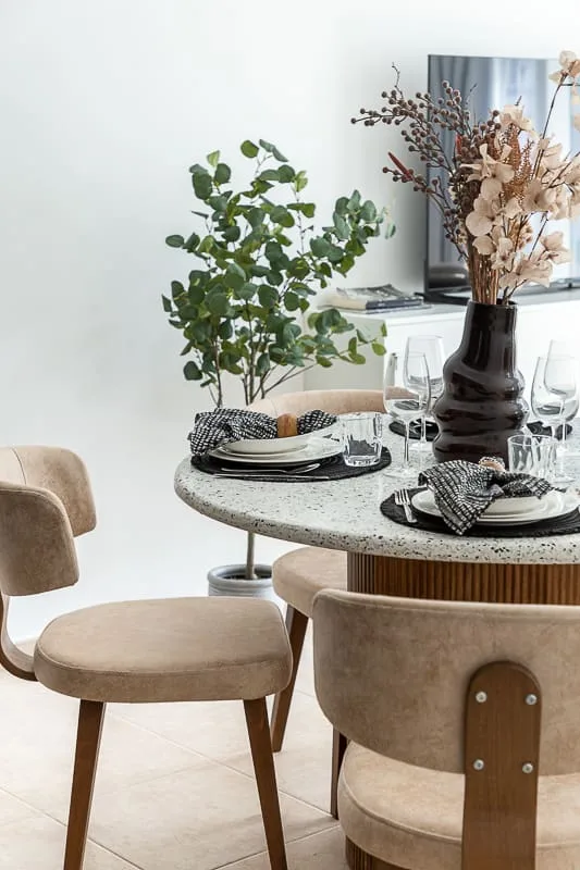 A dining area with a round table set with dishes and surrounded by upholstered seating.