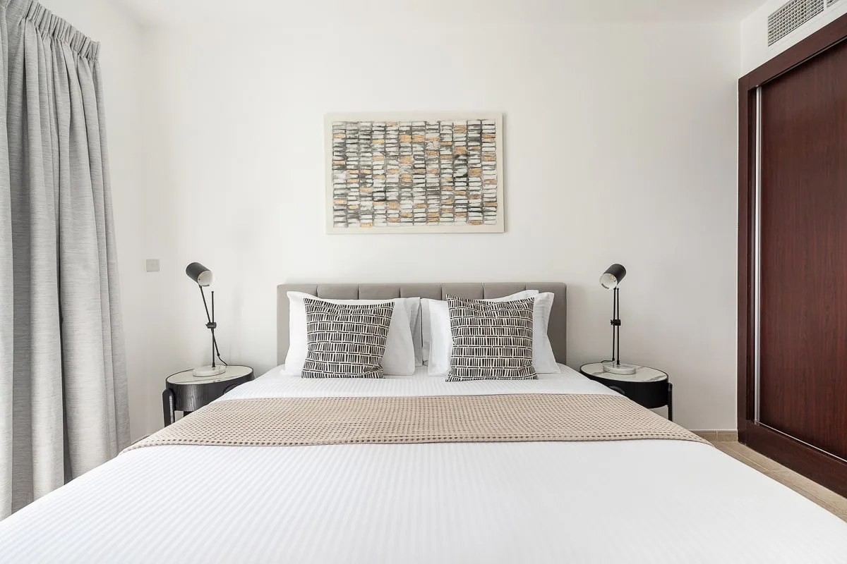 A bedroom with a neatly made bed, patterned pillows, and bedside lamps.