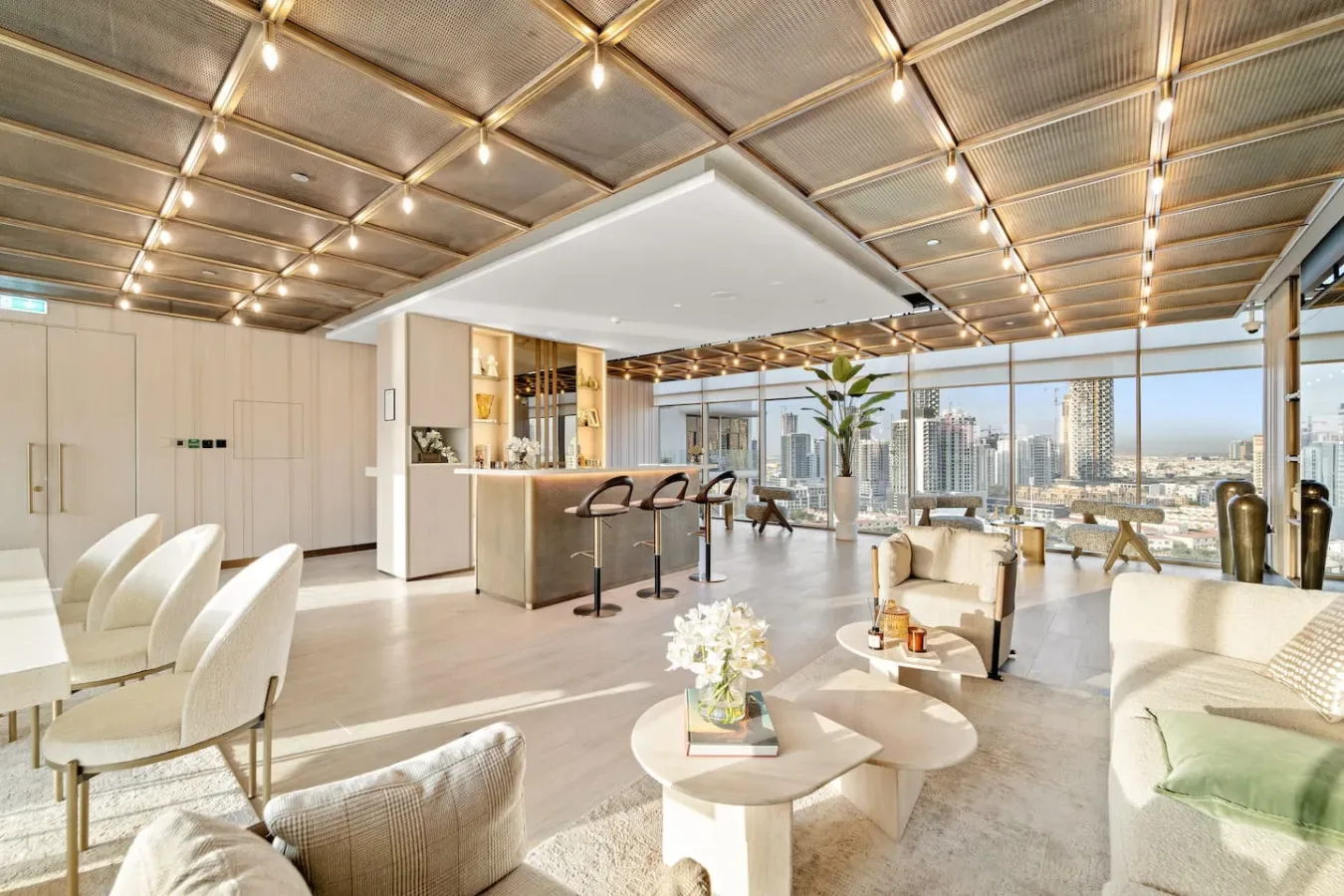 A bright lounge with seating, a bar counter, and floor-to-ceiling windows overlooking the city.
