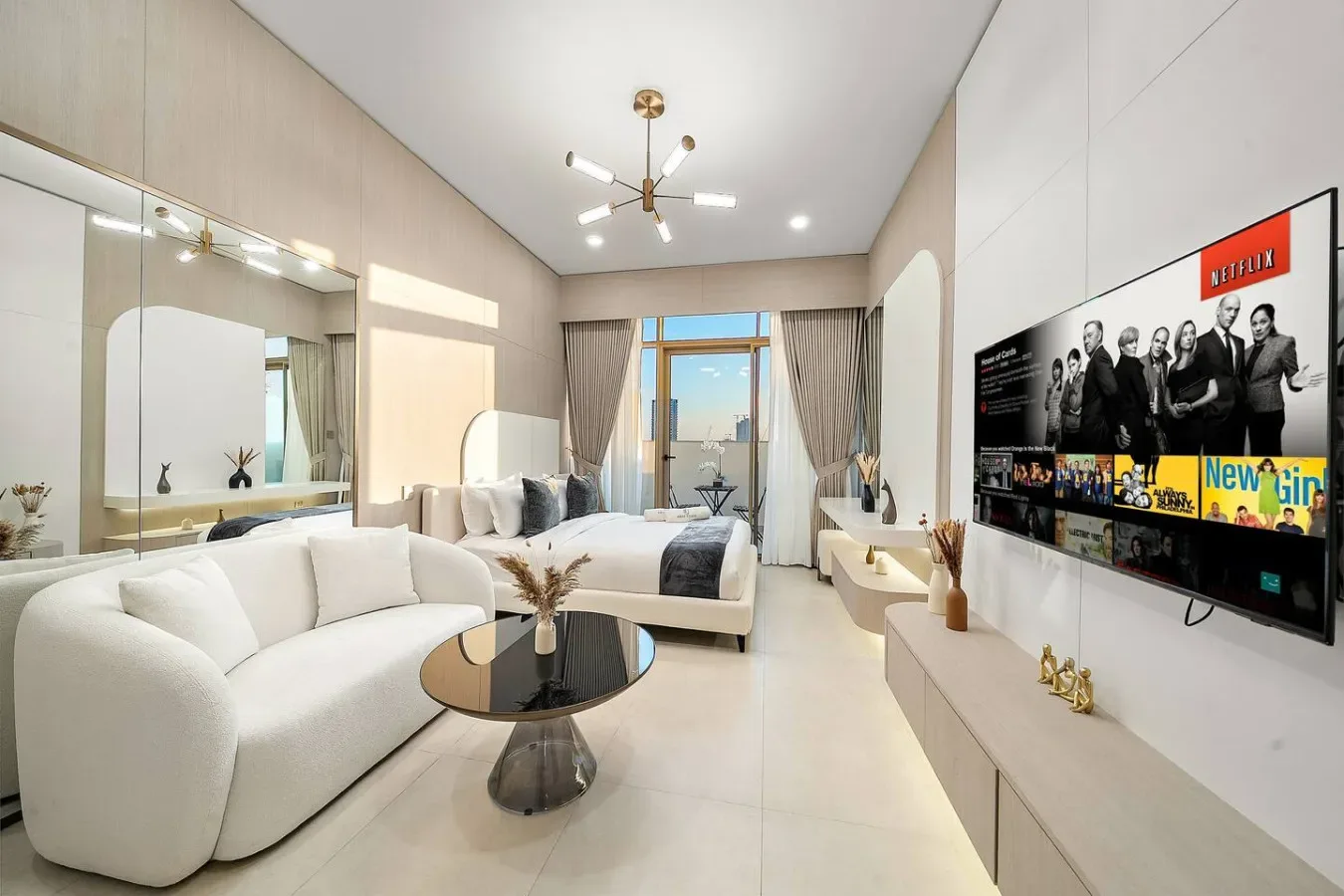 A bright bedroom and sitting area with a bed, seating, and a wall-mounted television.