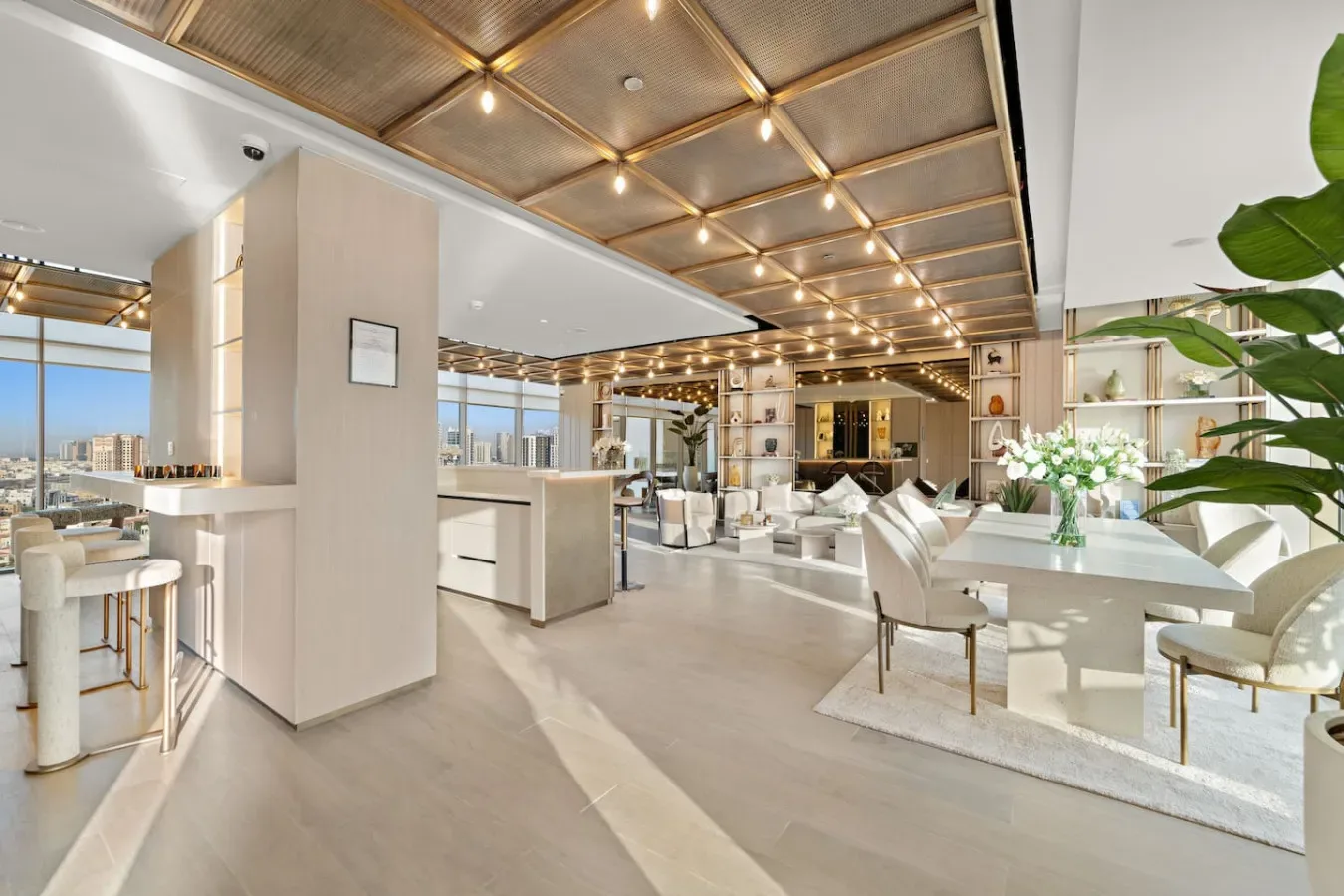 A bright open-plan living and dining area with large windows and a ceiling of warm lights.