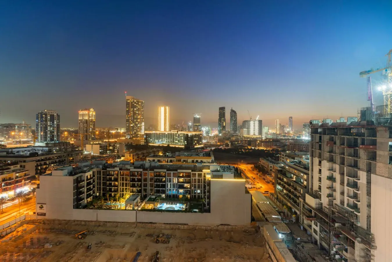 A city skyline at dusk, with illuminated high-rise buildings and streets.