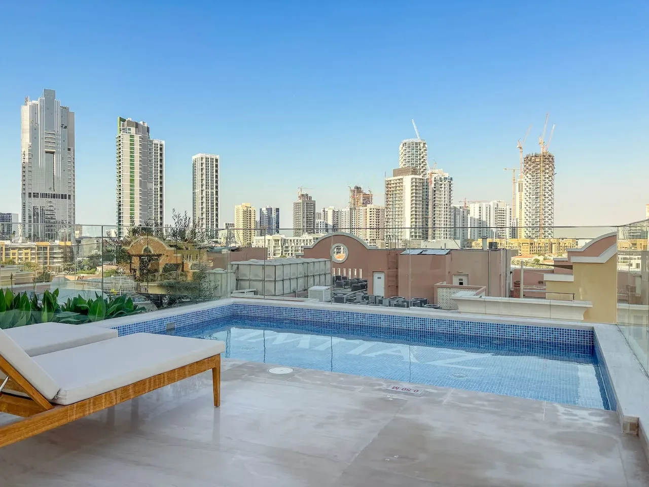 A rooftop swimming pool overlooks a city skyline, with cushioned seating beside it.