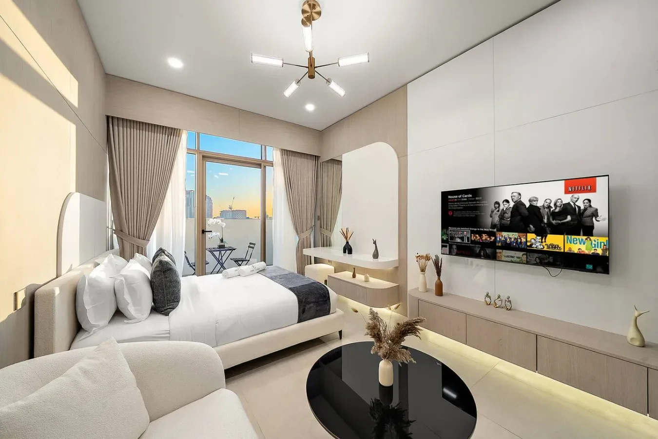 A bright bedroom with a bed, seating area, and large windows overlooking the city.