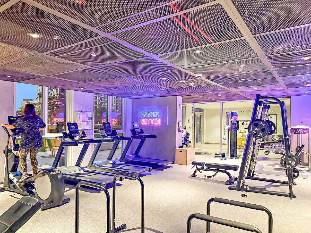 A gym with treadmills and strength-training equipment under colorful lighting.
