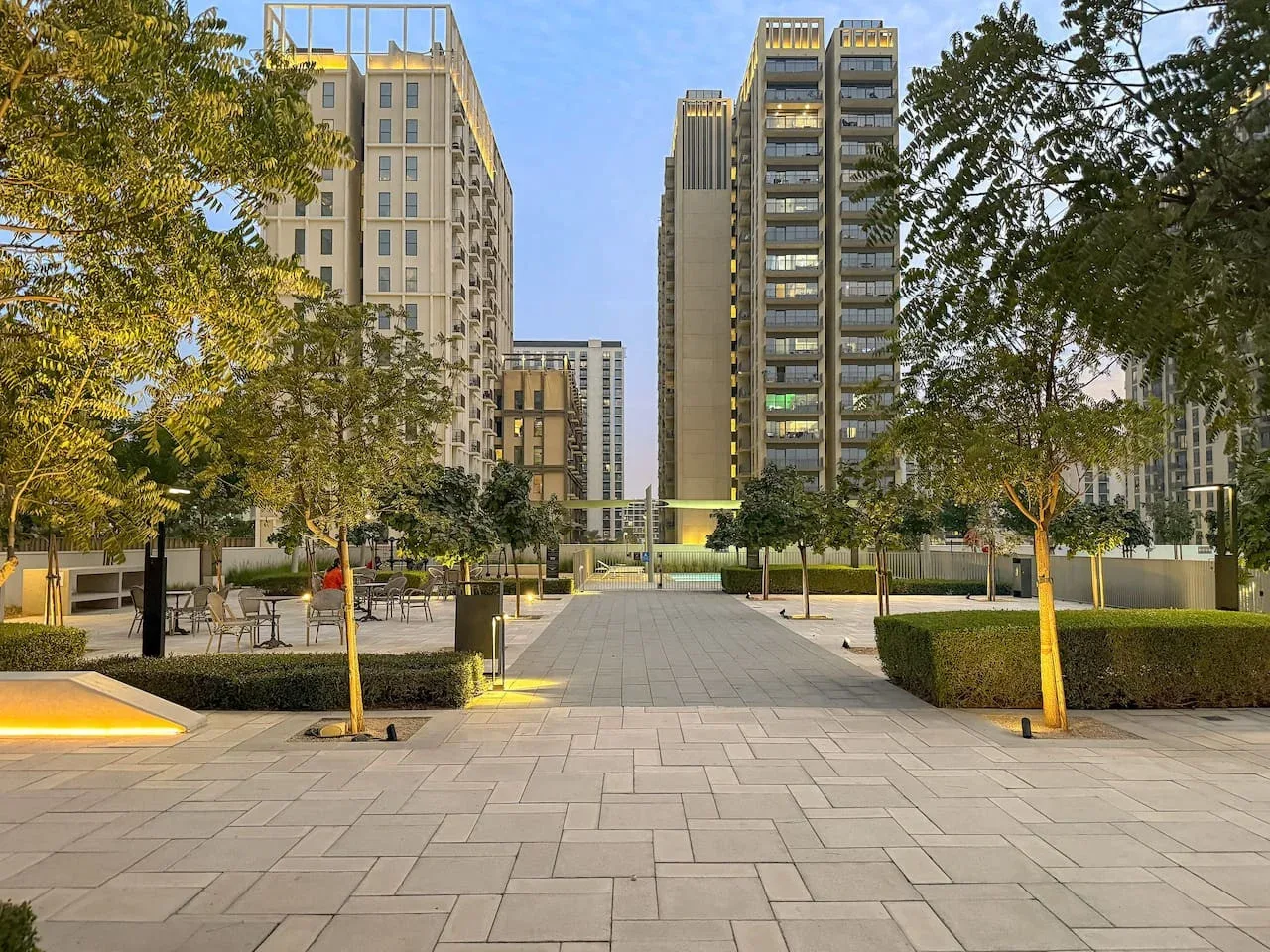 A paved outdoor courtyard with trees and tall buildings in the background.