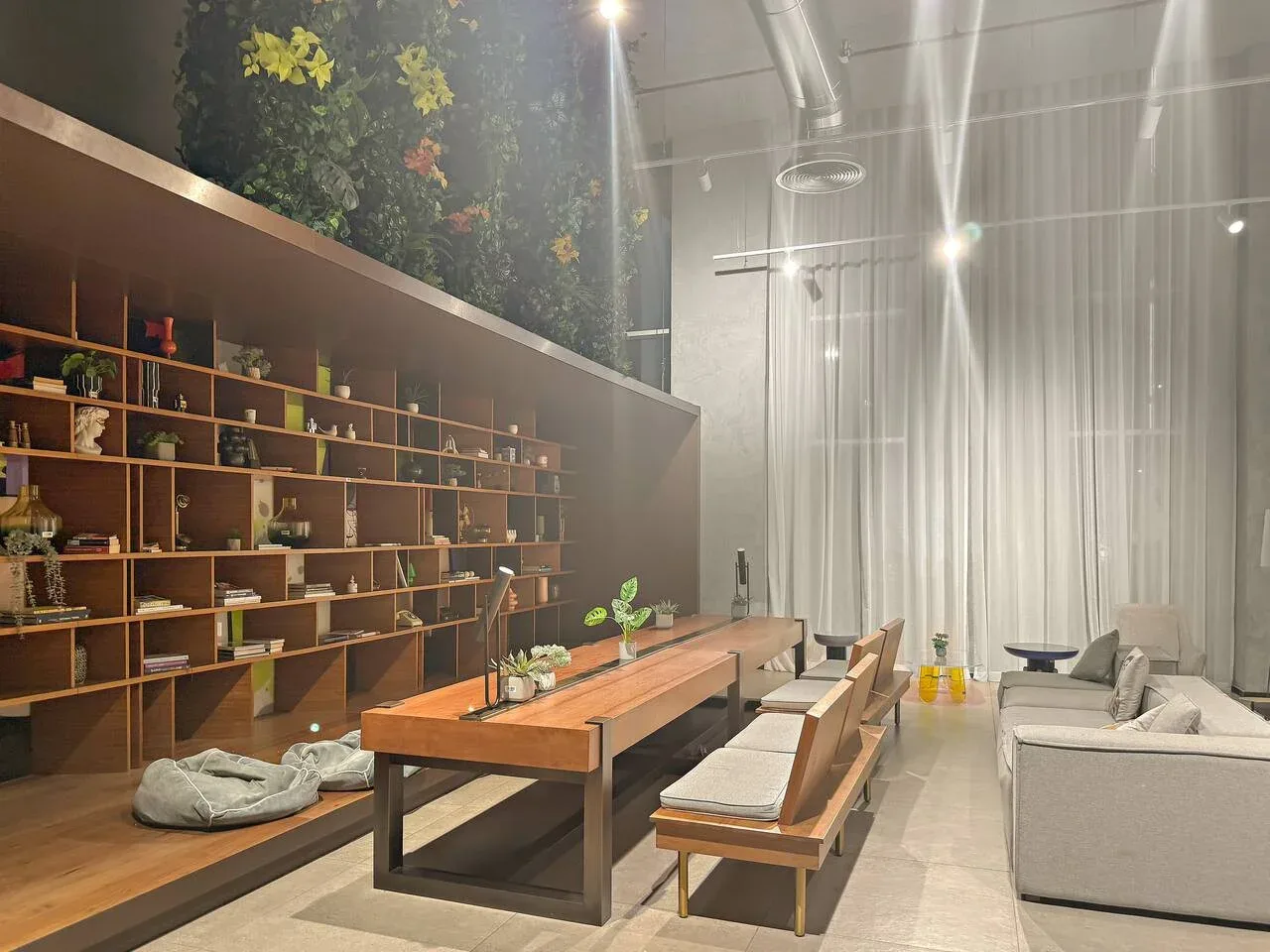 A modern lounge with long wooden shelving, a communal table, and seating.