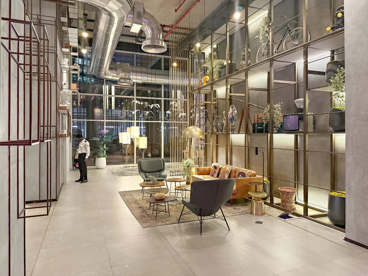 A modern lobby with seating arranged beside tall glass walls and metal shelving.
