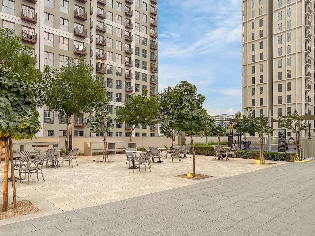 An outdoor paved courtyard between apartment buildings, with trees and seating.