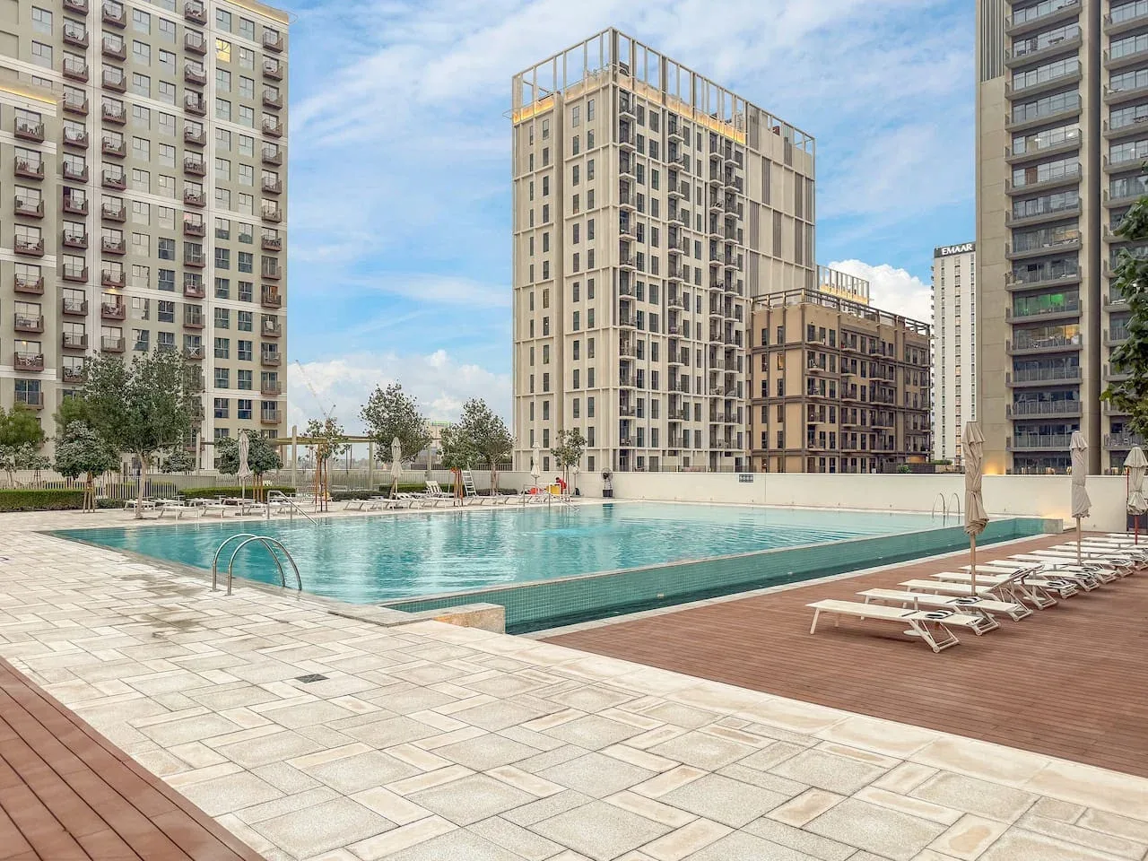 An outdoor swimming pool and surrounding deck sit among tall apartment buildings.