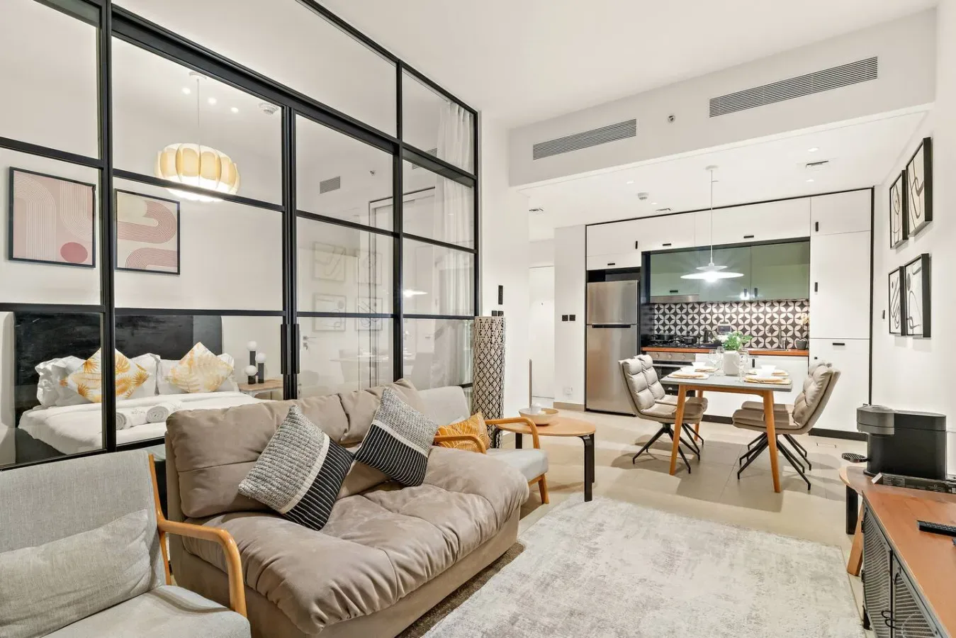 A living area with sofas beside a glass partition, opening onto a dining space.