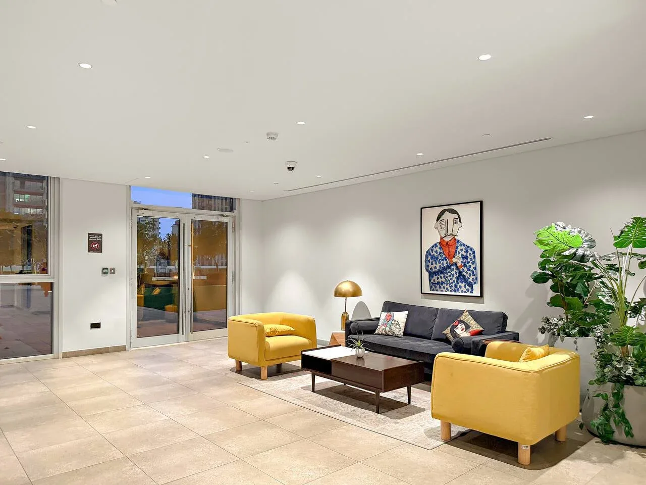 A bright lobby seating area with yellow armchairs, a dark sofa, and a coffee table.