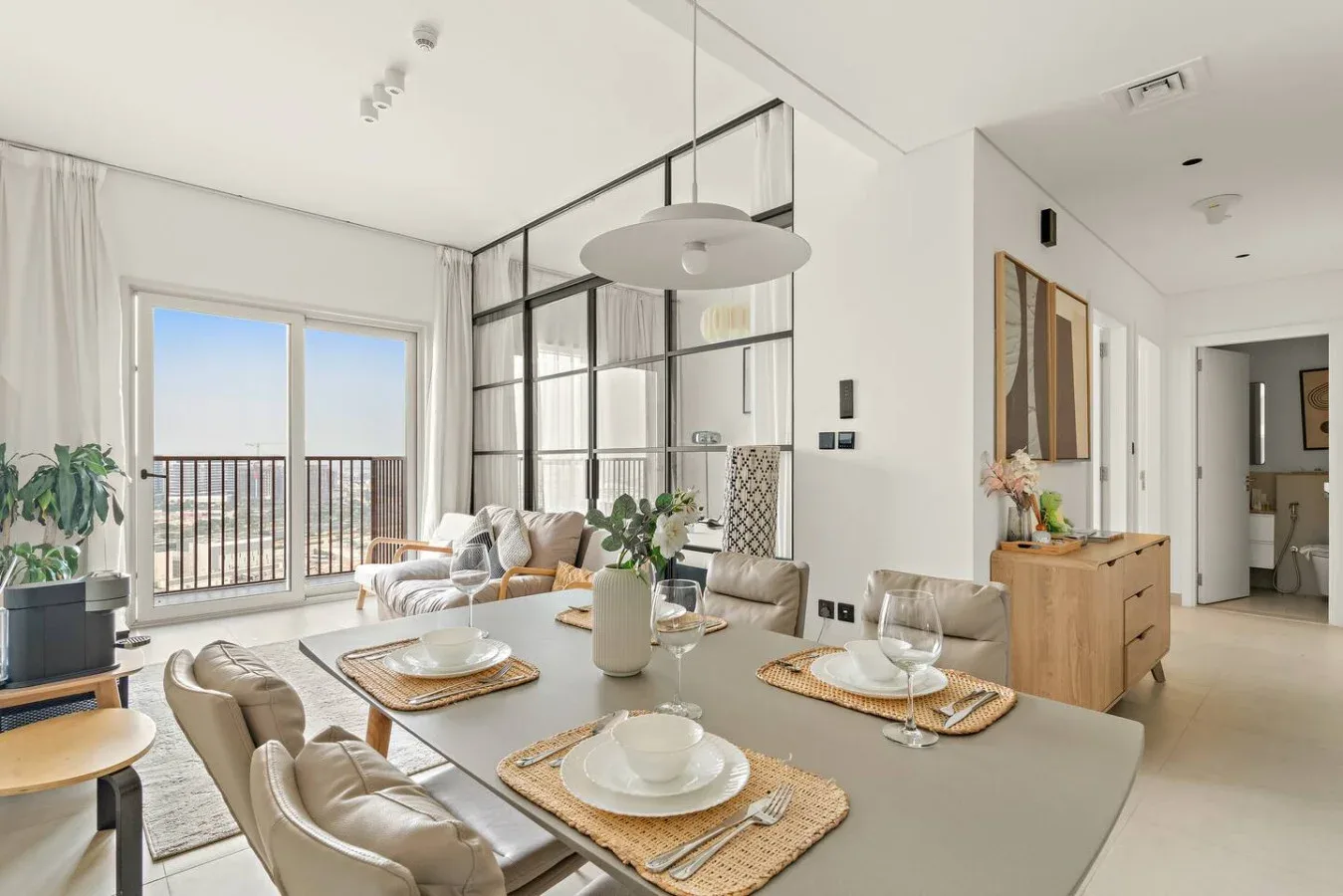 A bright dining and living area opens onto a balcony through large glass doors.