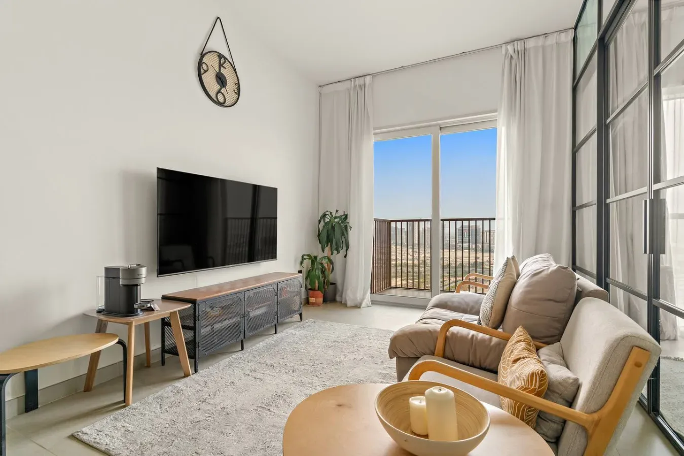 A bright living room with seating, a television, and large windows opening onto a balcony.