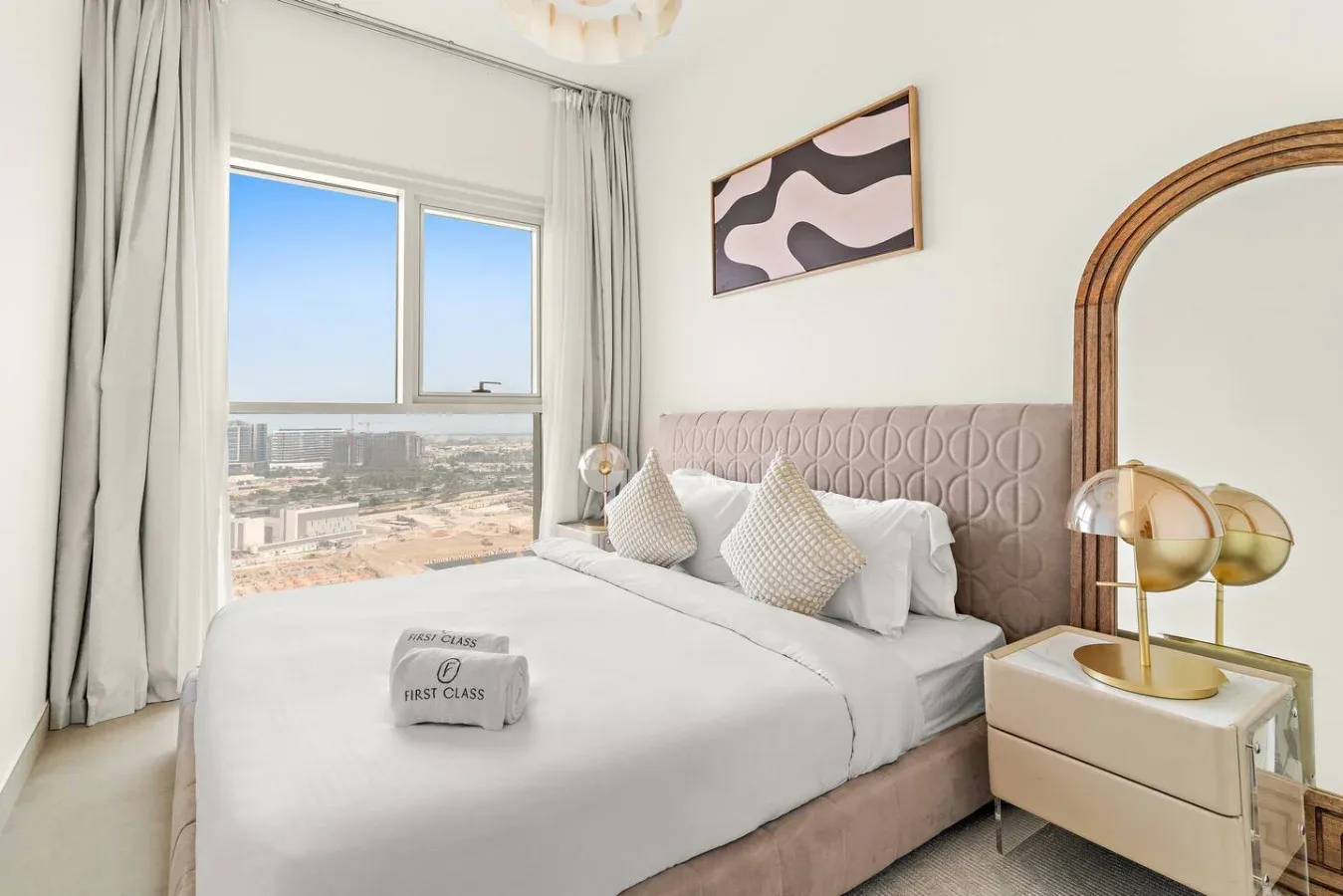 A bedroom with a neatly made bed beside a large window overlooking the city.