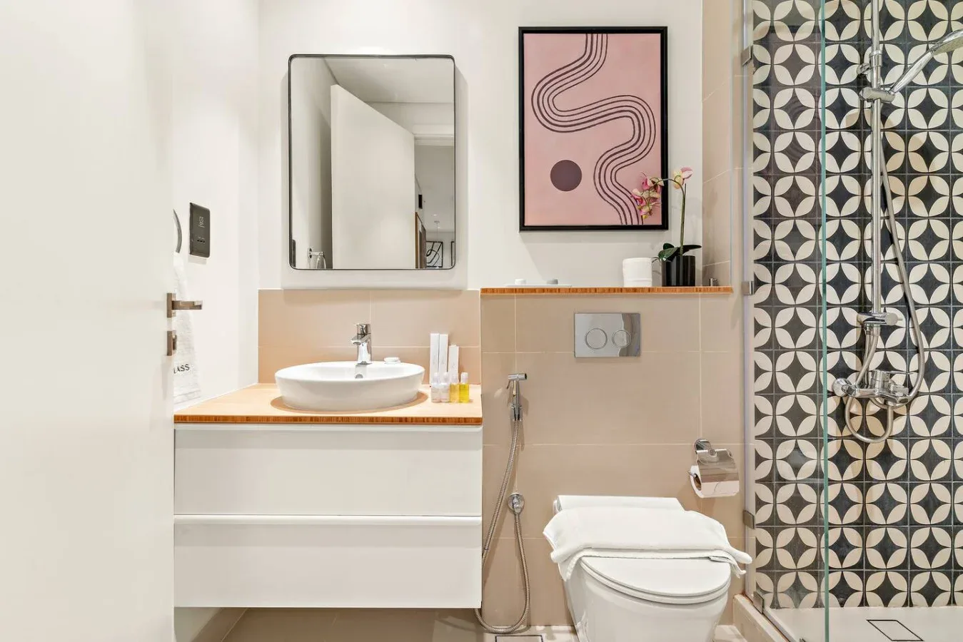 A bathroom with a sink, toilet, and patterned shower wall.