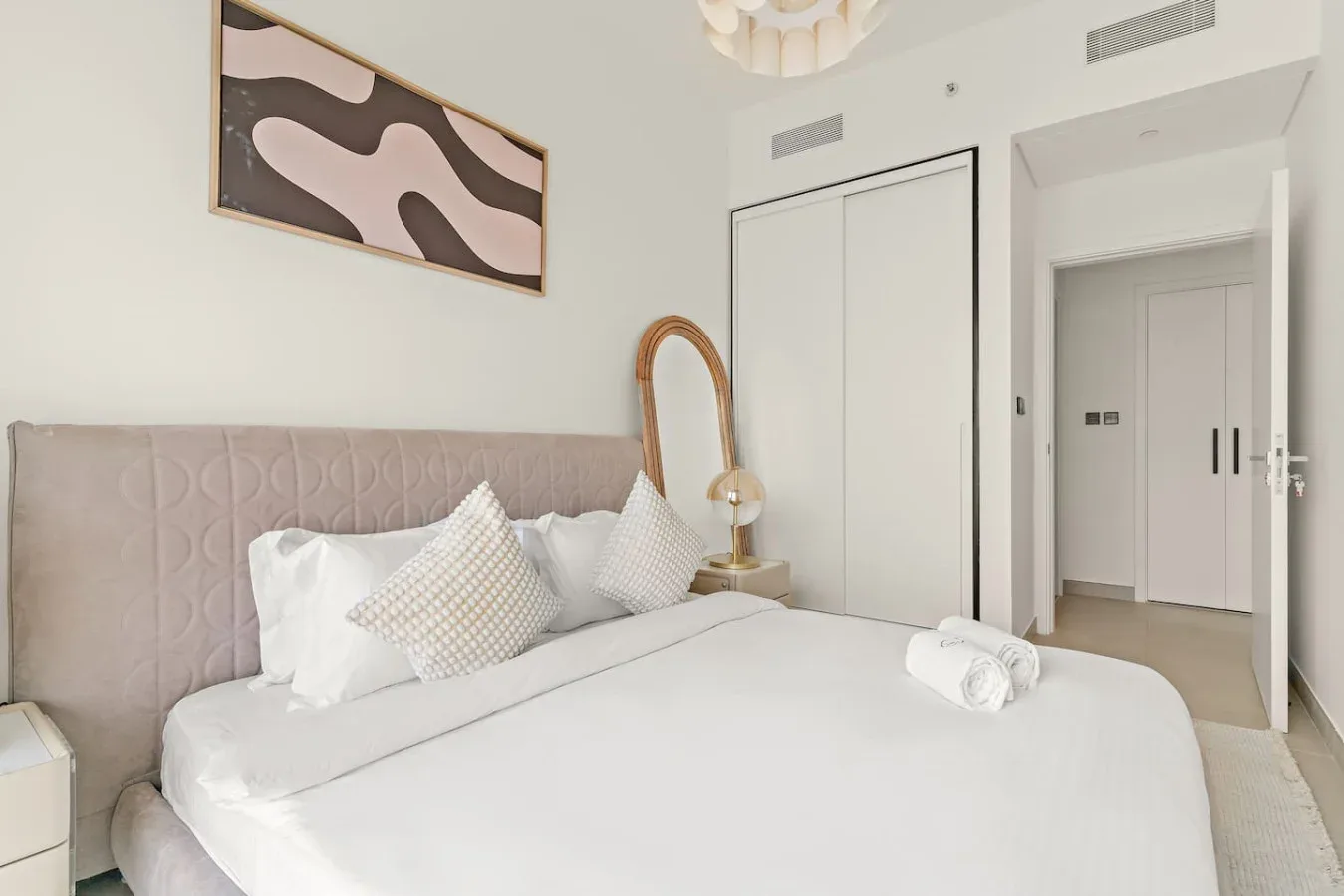 A bright bedroom with a neatly made bed and abstract wall art.
