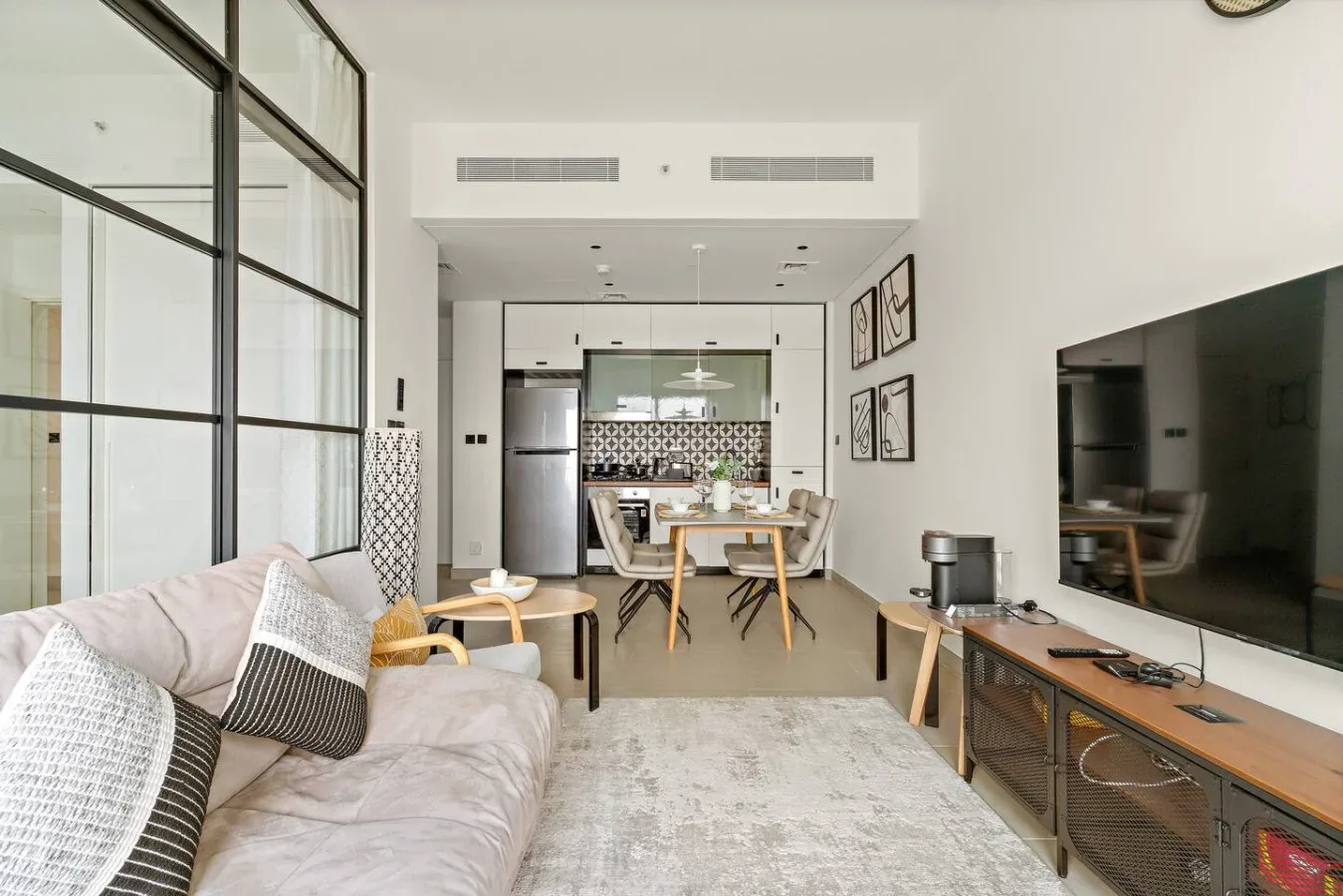 A bright living room with seating, a large television, and a dining area beyond.