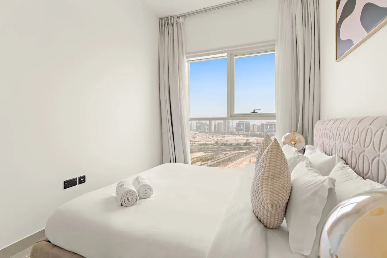 A bright bedroom with a neatly made bed beside a large window.