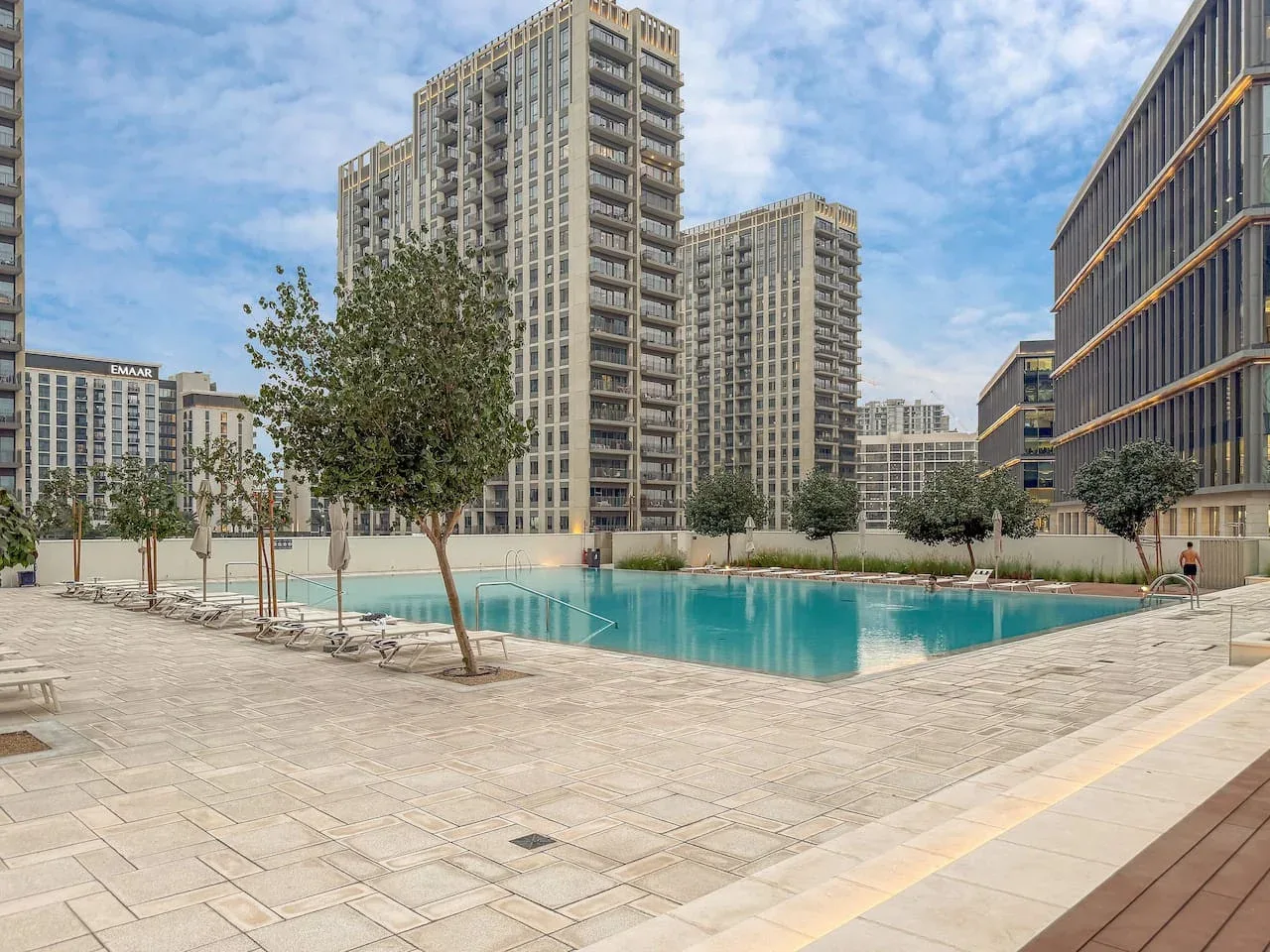 An outdoor swimming pool sits among paved walkways and tall apartment buildings.