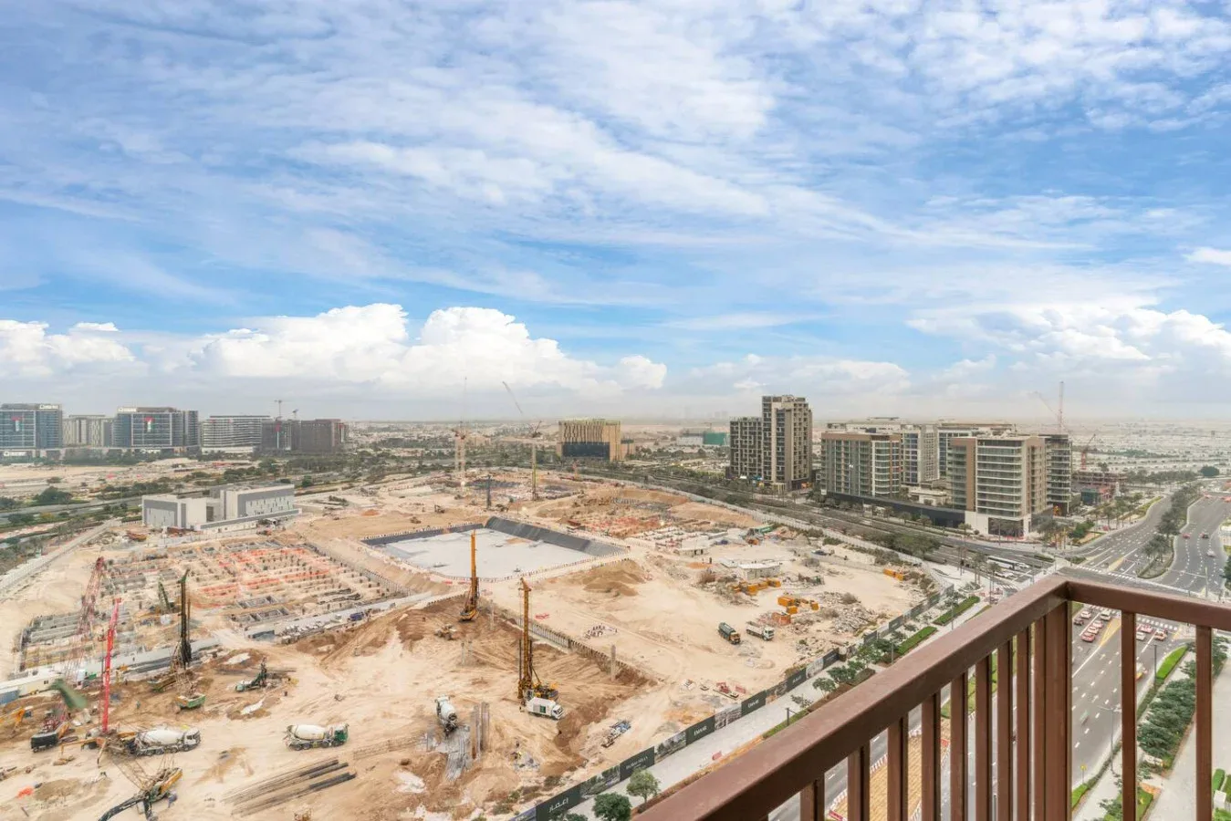 An urban construction site with cranes and buildings beneath a partly cloudy sky.