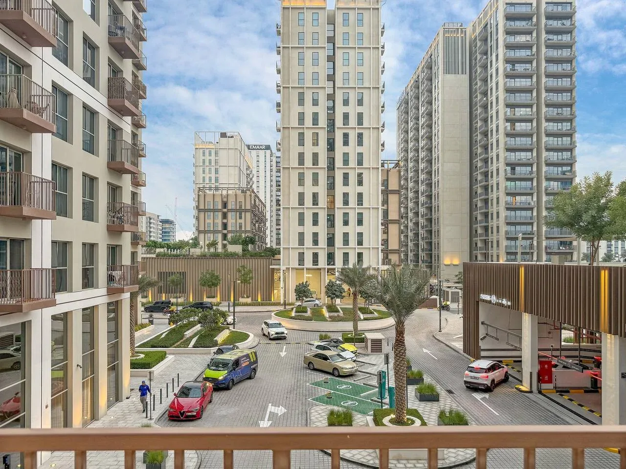 A courtyard between tall residential buildings, with landscaped paths and parked cars.