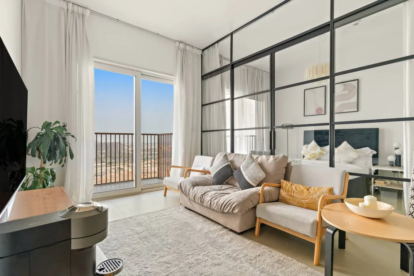 A bright living room with seating beside tall windows and a glass partition.
